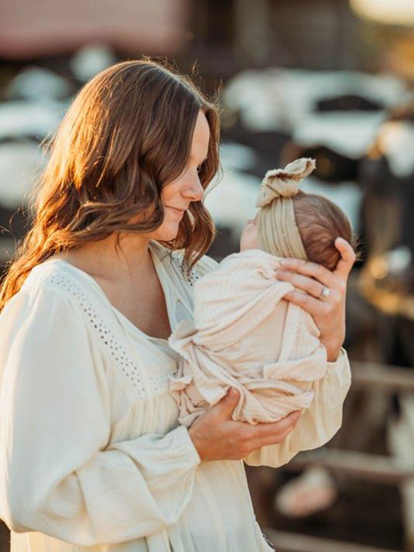 mother-and-baby-farm-photoshoot Mother looking lovingly at her swaddled newborn baby during a rustic outdoor farm photo shoot